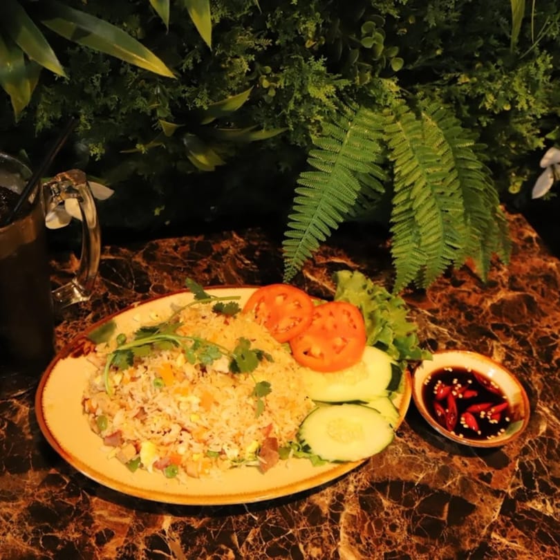 Vietnamese fried rice with vegetables, tomatoes, cucumbers, and a side of chili sauce.