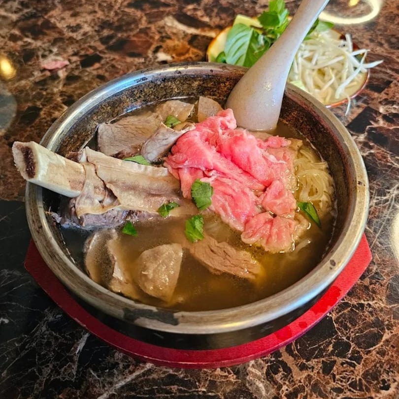 Viet Holic's pho with beef, bone marrow, and noodles in a metal bowl with a spoon.
