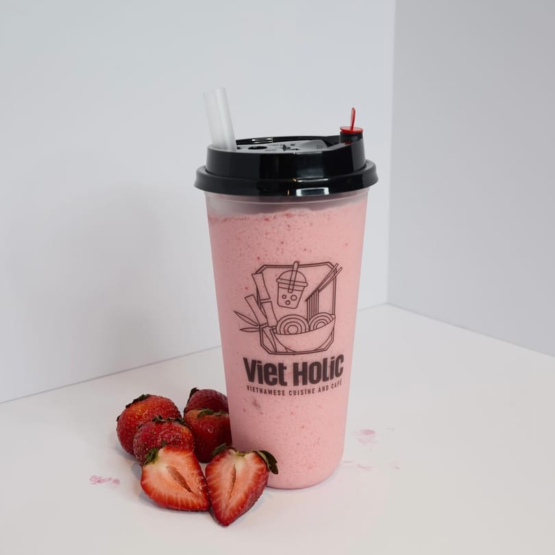 A Viet Holic strawberry smoothie with fresh strawberries on a white surface.
